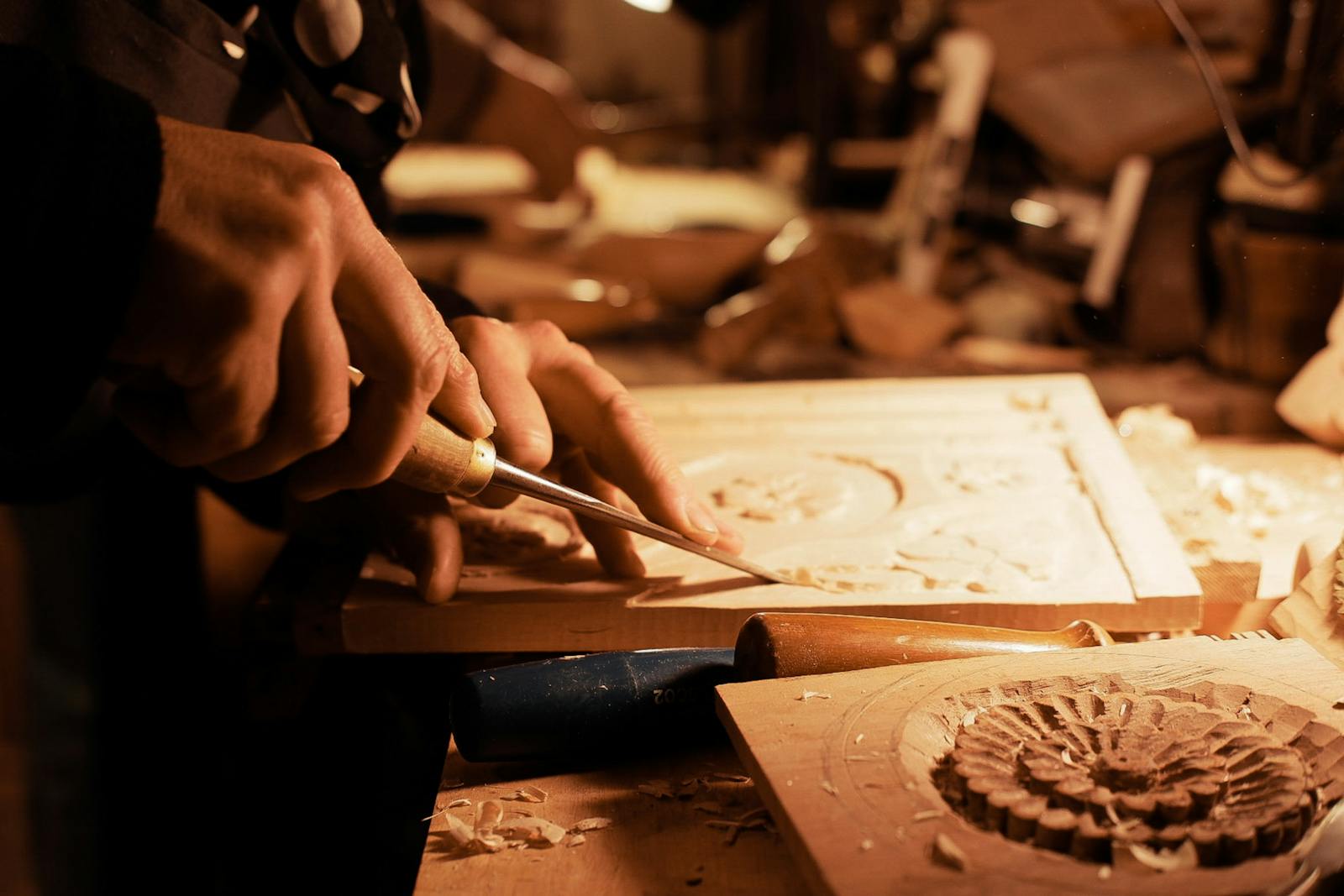 Craftsman carving intricate designs in wood under warm workshop light, atmospheric artisan scene