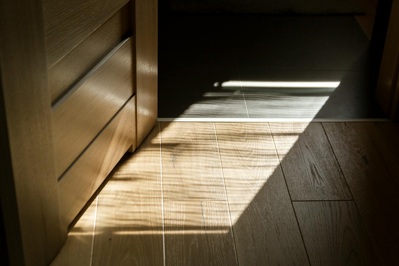 Sunlit shadow patterns on a wooden parquet floor, evoking the wood surface where every cutting board lives its life