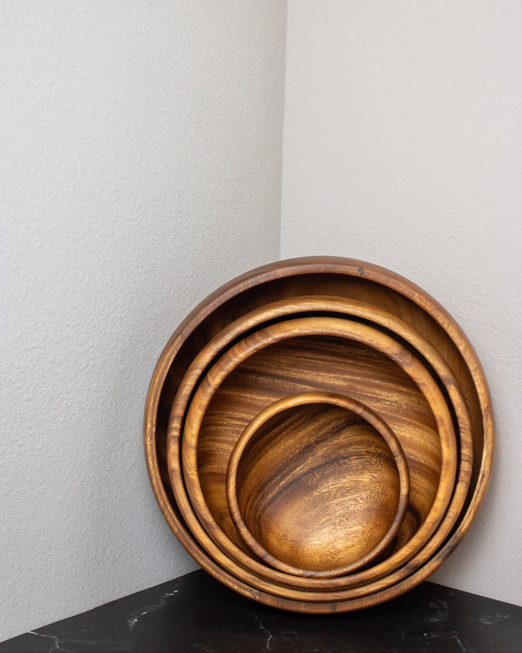 Set of three wooden bowls stacked on a black surface with a light gray wall background